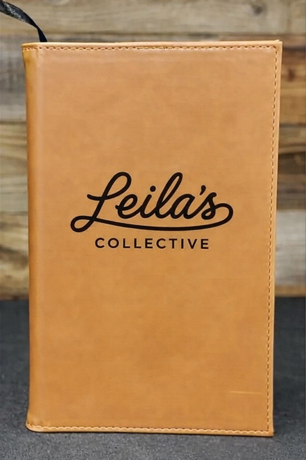Tan leather-bound book with 'Leila's Collective' branding on a wooden surface.