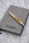 Gray notebook and pen set with 'Dr. Johnson' engraving on a marble surface