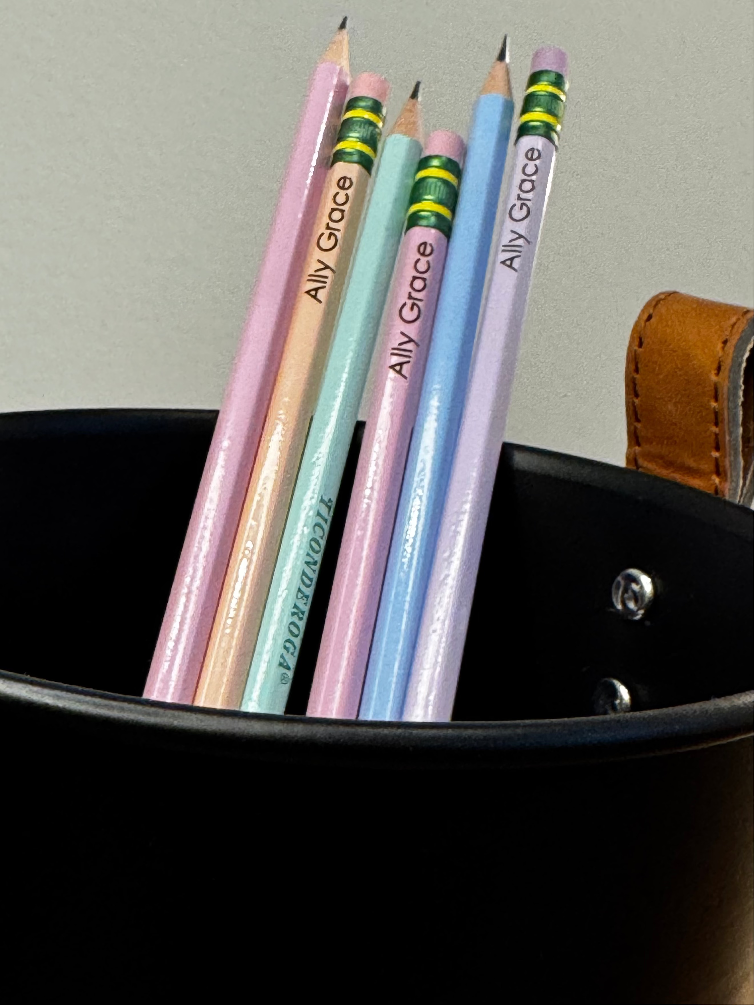 Four pastel-colored pencils with 'Ally Grace' printed on them, standing upright in a black cup.